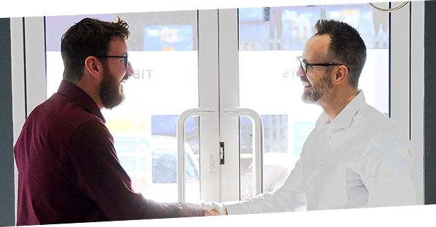 An image of two smiling men shaking hands, stood in the reception room at Tibbetts House.